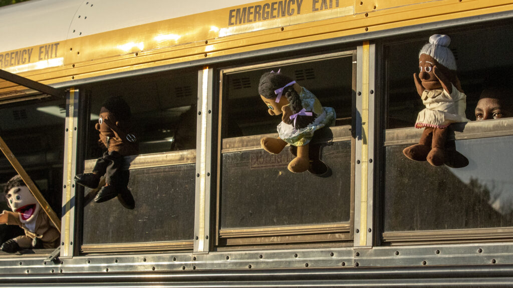 Puppets hang out of a school bus during a rehearsal of the mobile play "Sojourners Project: Busing" in the parking lot of the Rising Star Missionary Baptist Church in Aurora. Aug. 23, 2021.