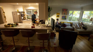 Paul Bindel (left to right) cooks as Melissa Kocelko, Mahalia Hunt and Alliegator the dog hang out on a couch in the co-op home they share in Athmar Park. Oct. 21, 2021.