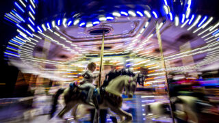 Kids and adults ride a merry-go-round set up at Lonnie Hanzon's Camp Christmas in Heritage Lakewood Belmar Park. Dec. 2, 2021.