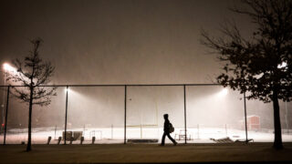 Denver East High School playing field floodlights illuminate falling snow and a lone pedestrian on 16th Avenue as a winter storm rolled through Denver Wednesday evening, Feb. 16, 2022.