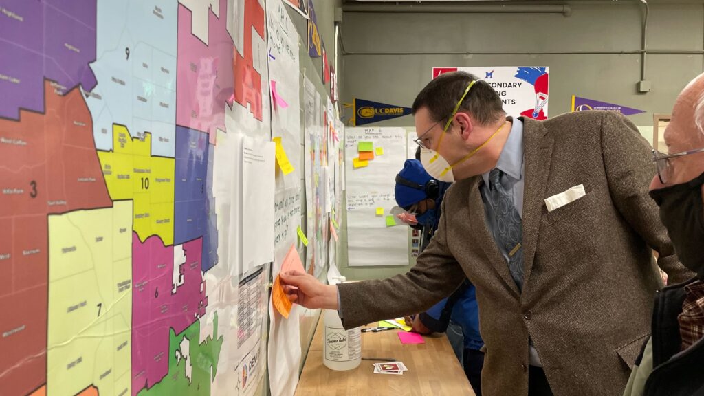 A man posts a note on a proposed Denver council district map during a redistricting meeting on Wednesday, Feb. 23, 2022, at Manuel High School. (Esteban L. Hernandez/Denverite)
