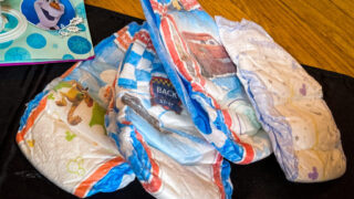 A close up of four disposable diapers with cartoon characters printed on them and a box of wipes nearby.