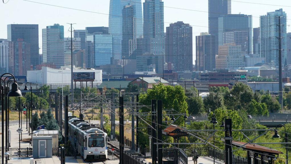 An RTD light rail train pulls out of the Decatur-Federal station, with the Denver skyline in the background, Aug. 12, 2022.
