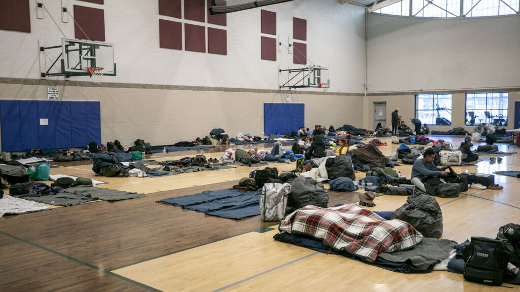 People who've arrived from the U.S. southern border hang out on bedrolls on the floor of a Denver rec center, the city's second emergency shelter. People were originally given cots, but a city spokesperson said they switched to mats to squeeze more people in when they neared capacity in late December. Jan. 6, 2023.