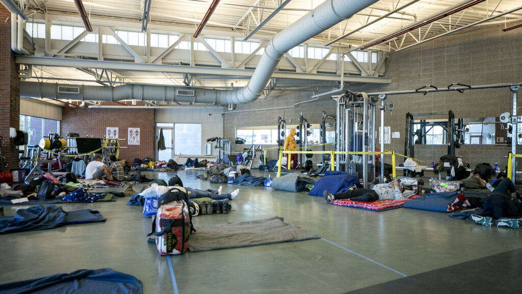 People who've arrived from the U.S. southern border hang out on bedrolls on the floor of a Denver rec center, the city's second emergency shelter. People were originally given cots, but a city spokesperson said they switched to mats to squeeze more people in when they neared capacity in late December. Jan. 6, 2023.