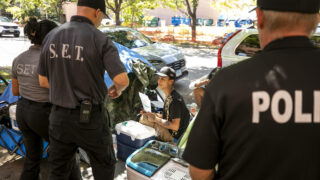 Denver Police officers and members of the city's Street Enforcement Team hand a sweep notice to Josef Steele, a resident of an encampment at Logan Street and 17th Avenue who was shot there by an uknown assailant just a day prior. Aug. 22, 2023.