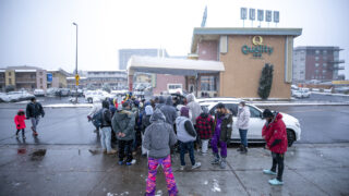 A crowd of migrants gathered around a car to accept food and clothing items being distributed outside of a shelter motel on Zuni Street. Oct. 28, 2023.