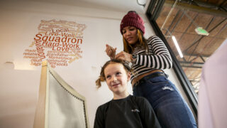 Janecy Rodriguez braids hair for Layla (5) as she and other asylum seekers run stalls to sell goods and make some money in an otherwise empty suite at Stanley Marketplace. Jan. 16, 2024.