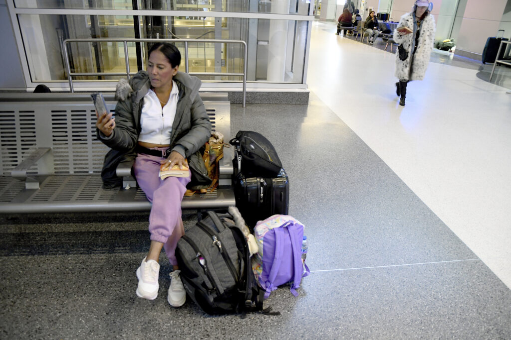 Sofia Roca waits on a bench for her Greyhound bus out of Denver, with a few bags on the ground.