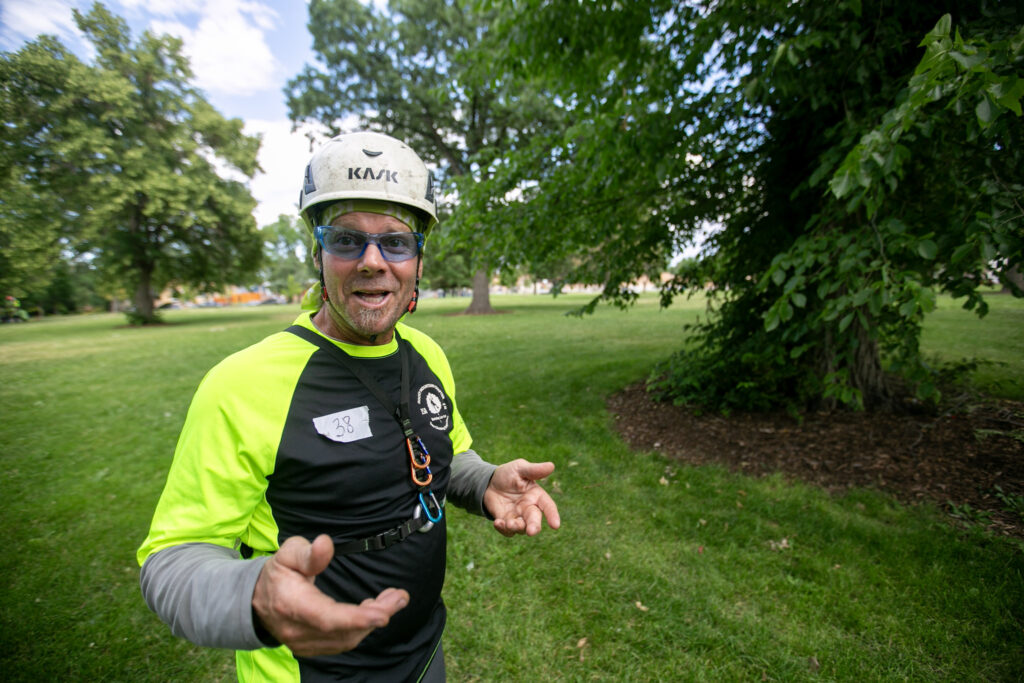 Patrick O'Meara gesticulates as he speaks, dressed in helmet, safety glasses, and vibrant green/yellow shirt.